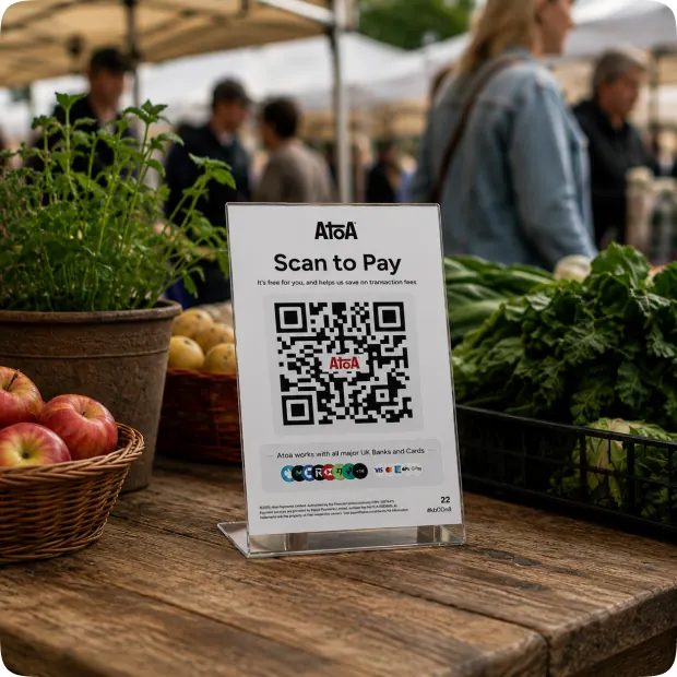 An Atoa Scan to Pay stand on a market stall among crates of fruit and vegetables